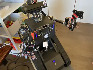 High angled view of the tracked robot with both jointed arms extended over its black chassis.