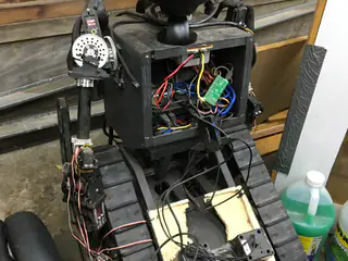 Slightly closer rear view of the robot's open wiring compartment beside its geared shoulder joint.