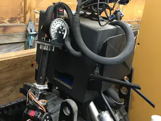 Wider rear view of the robot's cable loop, side enclosure, jointed arm, and tracked base.