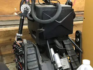 Rear view of the enclosed robot body and left arm beside the tank tread and motor.