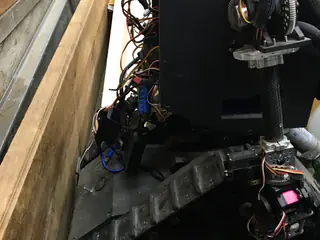 Low side view showing the robot's tread, exposed cabling, black enclosure, and arm hardware.