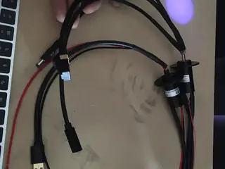 Hand holding looped power and data cables attached to two cylindrical rotary connectors beside a laptop.
