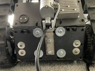 Centered rear close-up of the drive assembly, motor, cable, mounting bolts, and two tank treads.