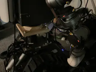 Dark lower-angle view of the arm's rotary joints, wooden mounting plate, and small status lights.