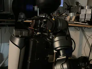 Dim close-up of the robot's upper arm joints and side enclosure with a workstation beyond.