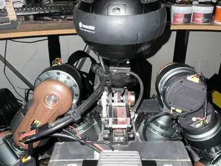 Flash-lit upper view of the camera head, twin shoulder joints, wooden arm plates, and neck gearing.