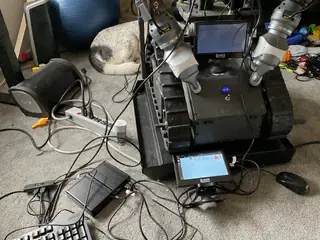 Tracked base with mounted monitor and tablet, cables across the carpet, and a curled dog behind.