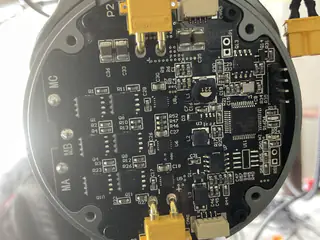 Circular black circuit board with dense electronic components, printed labels, and yellow connectors.