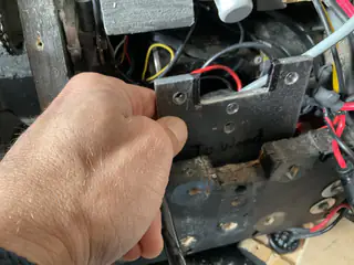 Hand holding a black steel bracket above the robot's open chassis and exposed wiring.