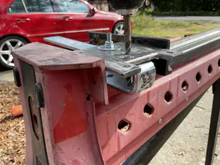Power drill aligned over a bolted metal rail clamped to a red workbench.