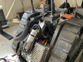 Angled overhead view of the tracked base with gray motor, coiled braided hose, and metal fittings.