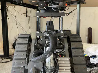 Front view of the tracked base with coiled hose and motor centered between the treads.
