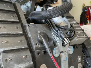 Close side view of a tank tread, gray motor, bolted bracket, and braided cable.