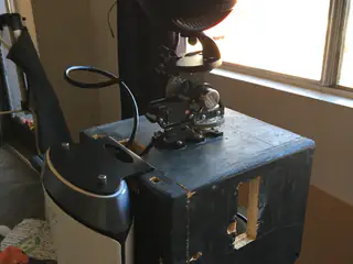 Compact camera assembly mounted on a worn blue box beside a sunlit window.