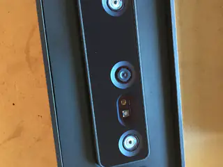 Top-down close-up of a black stereo depth camera with three blue-ringed lenses on wood.