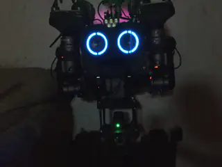 Dark frontal view of the robot illuminated by two blue ring lights and a green status light.