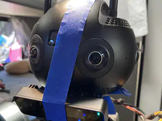 Close left-side view of the spherical head with a vertical blue tape strap and paired sensors below.
