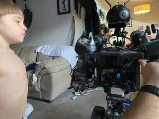 Young child faces the humanoid robot in a living room, with an adult arm at right.