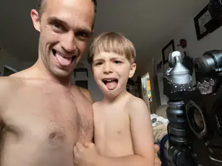 Adult and child stick out their tongues beside the robot, whose arm fills the right edge.