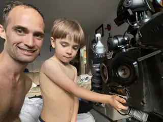 Smiling adult and child beside the robot as the child reaches toward its circular chest sensor.