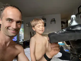 Smiling adult beside a child touching the robot's rectangular forearm in close framing.