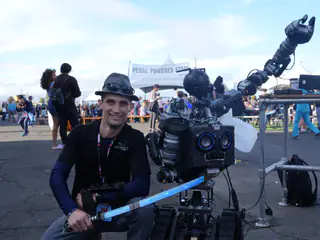 Exhibitor and blue-eyed tracked robot pose together, holding a long blue foam sword.