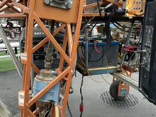 Orange steel robot frame surrounds a battery, wiring, hoses, and a small metal cylinder.