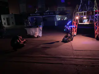 Small tracked robot faces an amber-lit orange gantry while a person crouches nearby at night.
