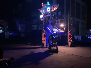 Centered tracked robot sits beneath the illuminated dragon head, casting a long nighttime shadow.