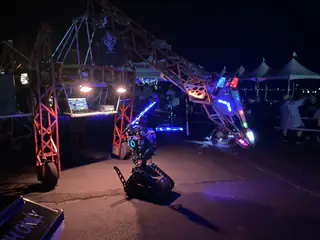 Wide nighttime view shows the dragon head extended diagonally over the blue-lit tracked robot.