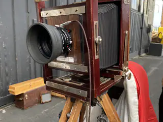 Vintage large-format bellows camera with a wide lens stands on a wooden tripod.
