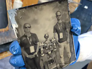Closer front-facing glass plate portrait shows two people standing on either side of a robot.