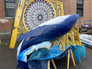 Blue whale model rests above a wave-shaped display in front of a painted cathedral backdrop.