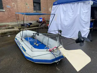 Small inflatable sailboat carries a metal mast frame and oversized white propeller outdoors.