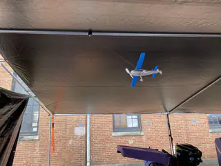 Small blue-and-white model airplane hangs by thin lines beneath a dark booth canopy.