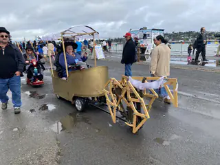Wooden articulated walking mechanism extends from a gold vehicle as fairgoers gather nearby.
