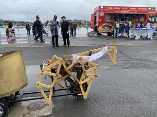 Close side view shows the jointed wooden leg assembly attached to the gold vehicle.