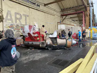 Long cylindrical steampunk art vehicle stands inside the exhibition hall as an attendee watches.