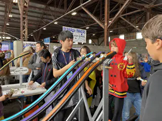 Children gather around a four-lane wooden race ramp holding round wooden cars.