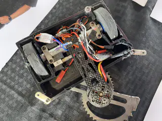 Open robot chassis reveals layered gears, motors, wiring, and a curved metal weapon.