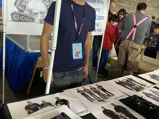 Exhibitor stands behind a table displaying small robots, tools, and printed team materials.
