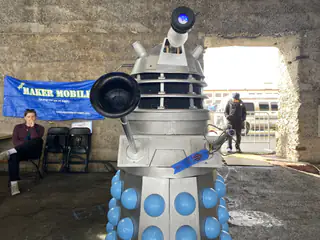 Gray Dalek replica extends its black plunger arm toward the camera.