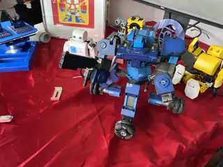 Blue humanoid robot stands amid colorful toy robots on a red display table.