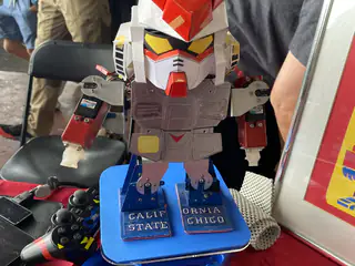 Blocky red-and-white humanoid robot stands on a blue California State Games base.