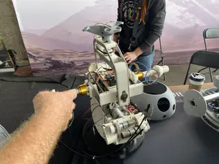 Person points a yellow handheld controller toward a partially disassembled white spherical droid.