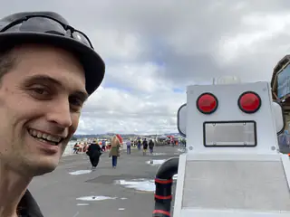 Smiling attendee takes a selfie beside a white robot with two red circular lights.
