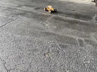 Tiny orange remote-control car sits alone on broad cracked asphalt.