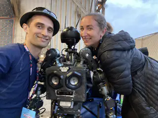 Closer selfie frames two smiling adults beside the black robot with its head still turned.