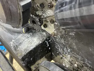 Rotary tool bit contacts a small sprocket beside the tread, with metal shavings across the frame.