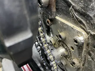 Chain wrapped around a small drive sprocket mounted to a drilled metal plate.